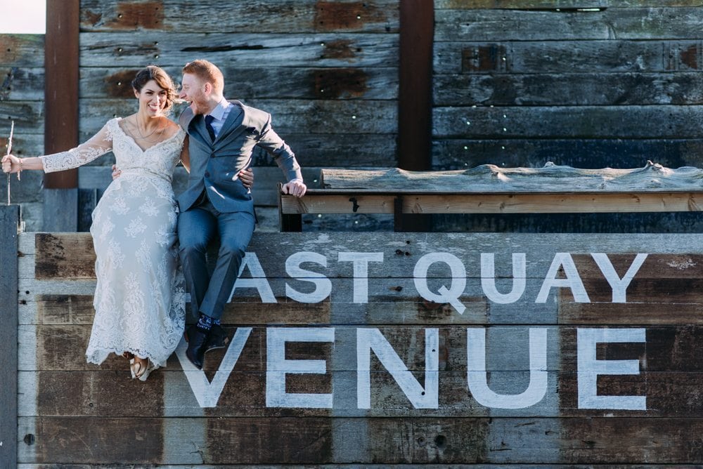 bride and groom sitting on a sign at east quay wedding venue in kent