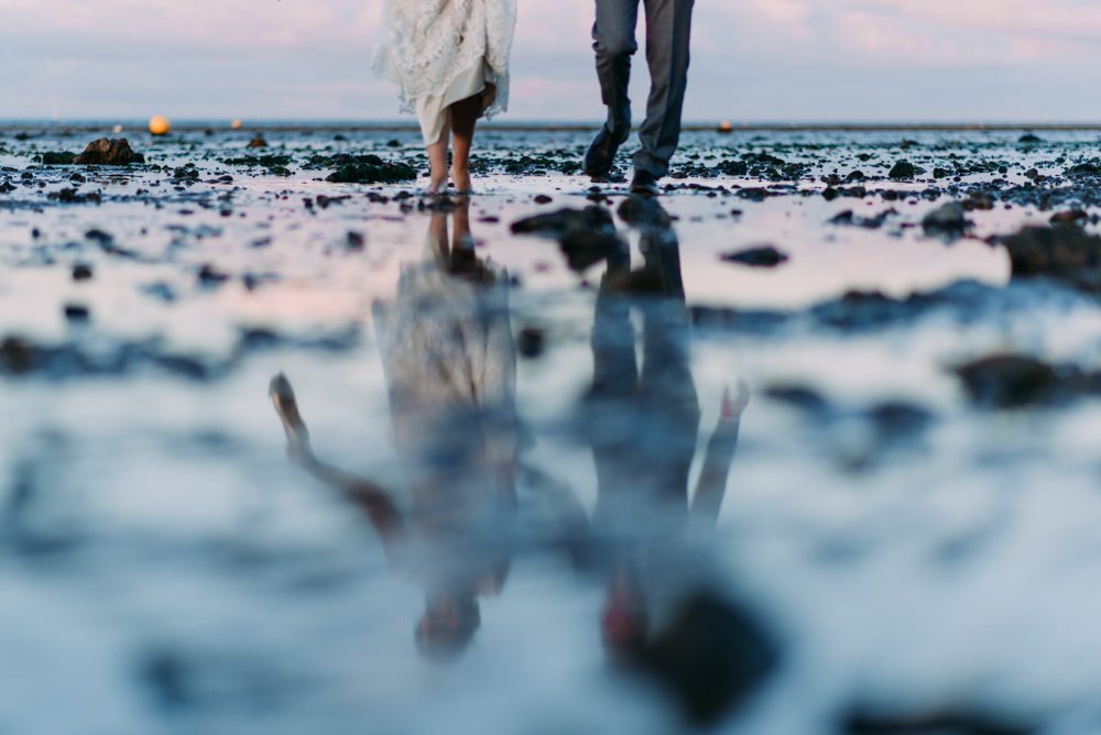 bride and groom feet in the sea with a reflection in the sand at sunset at east quay wedding venue in kent
